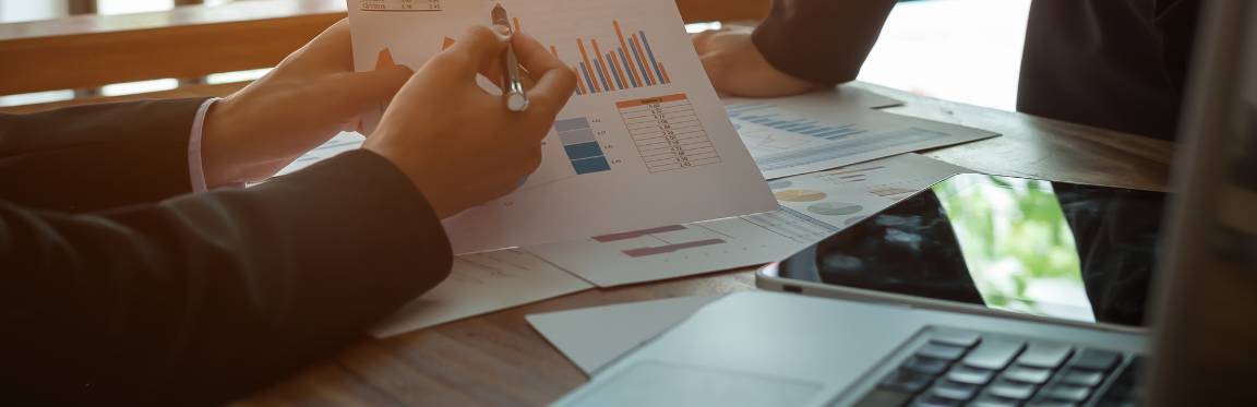 Two individuals, at a table, reading through graphs and charts displaying data.