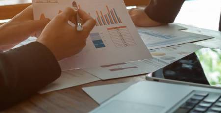 Two individuals, at a table, reading through graphs and charts displaying data.