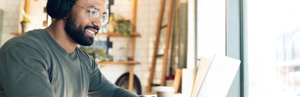 A person wearing headphones sits at a table and works remotely on their laptop.