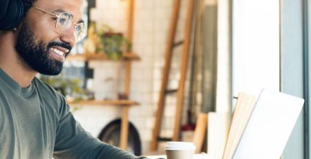 A person wearing headphones sits at a table and works remotely on their laptop.