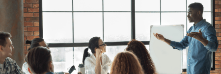 A man enthusiastically presents to a group of people during a corporate meeting.