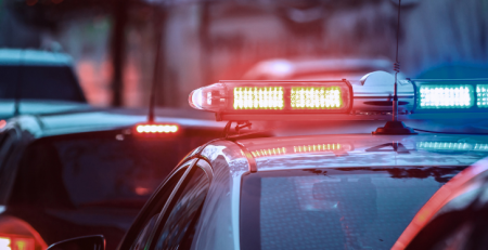 A police siren on top of a police car standing in a line of cars.