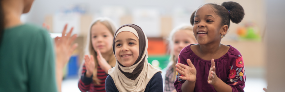 A group of children smile and follow their teacher's hand movement.