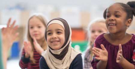 A group of children smile and follow their teacher's hand movement.