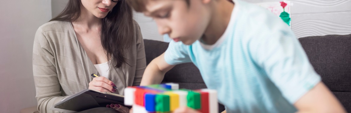 A school psychologist sits with a child and takes notes as the child plays with Lego.