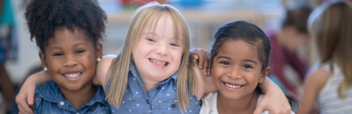 Three young girls smile and pose for a photo. The girl in the middle has her arms around the two girls beside her.