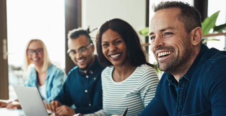 Four colleagues sit next to each other at a conference table and smile.