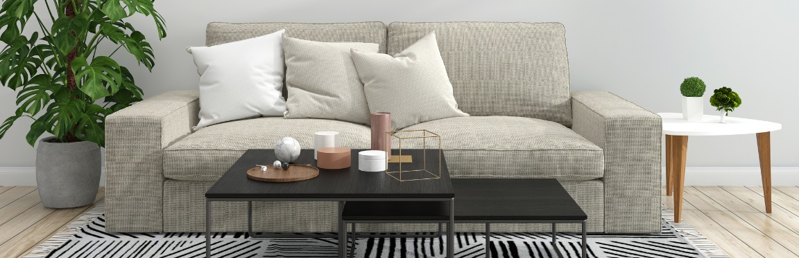 A couch with a coffee table in front of it and plants on both sides of it.