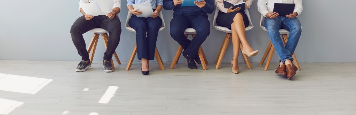 A group of job applicants sit in a row in a waiting area.