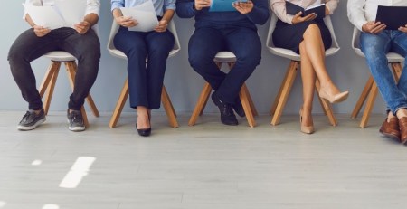 A group of job applicants sit in a row in a waiting area.