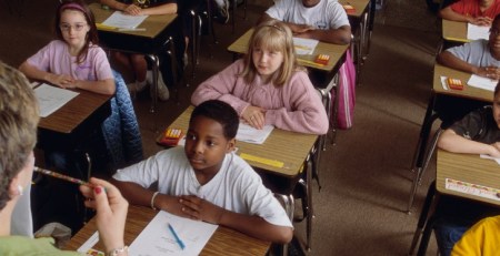 A classroom of students sit at their desk, attentively listening to their teacher.