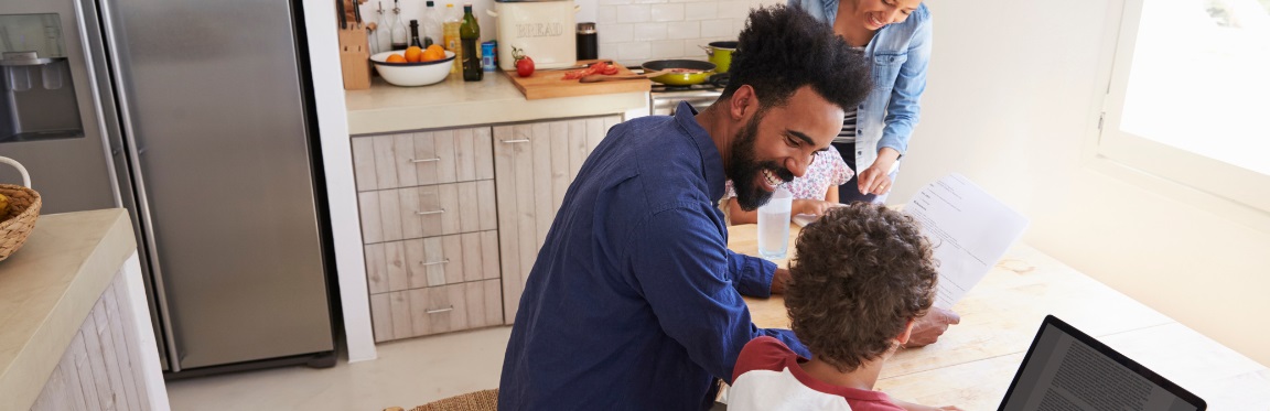 A family sits at the kitchen table. Mom and dad help the kids with homework.