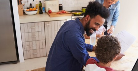 A family sits at the kitchen table. Mom and dad help the kids with homework.