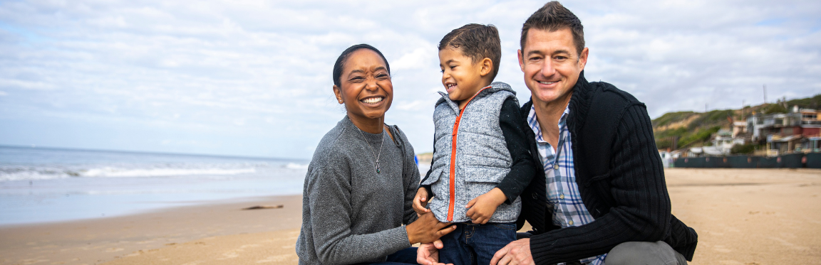 A mother, father and their young child smile on the beach.