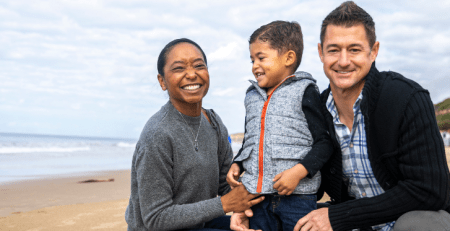 A mother, father and their young child smile on the beach.