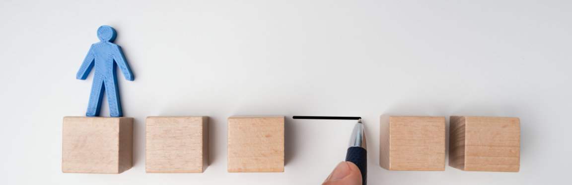 Five wooden blocks are lined up with a gap between them. A blue paper cutout of a person stands on the first wooden block.