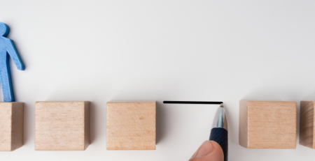 Five wooden blocks are lined up with a gap between them. A blue paper cutout of a person stands on the first wooden block.