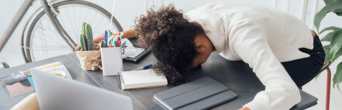 A woman rests her head on her desk in exhaustion.