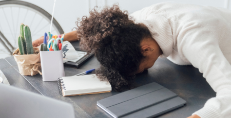 A woman rests her head on her desk in exhaustion.