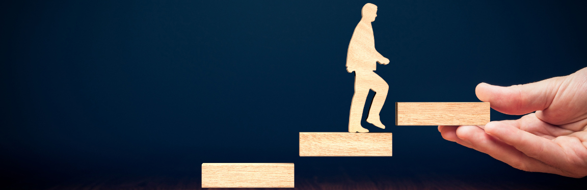 A wooden cut out of a person walking up a set of wooden blocks that are held out by a hand.