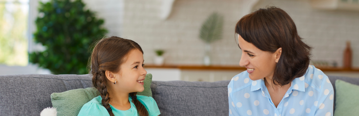 A young girl sitting on a couch next to a practitioner. They smile at each other.