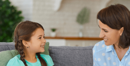 A young girl sitting on a couch next to a practitioner. They smile at each other.