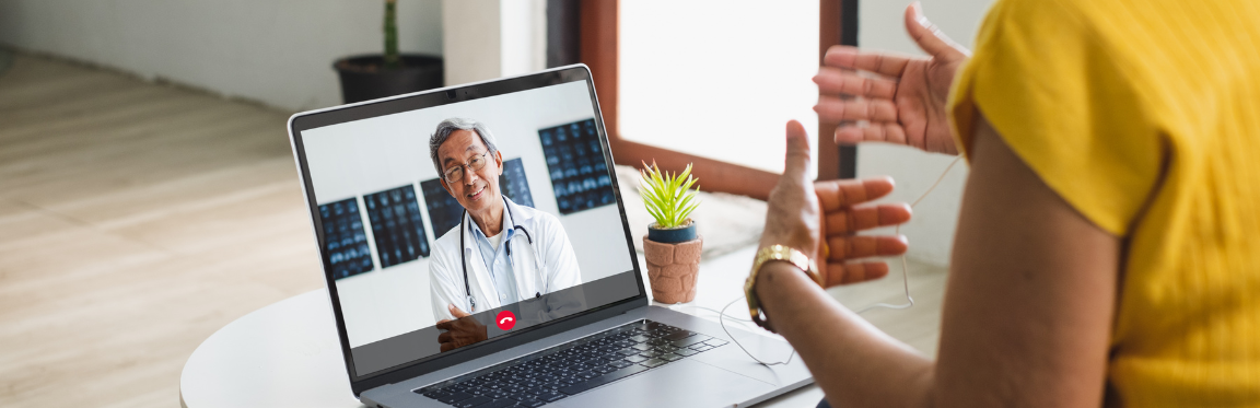 A doctor and their patient talk over a video call. The doctor is seen listening and smiling on screen.