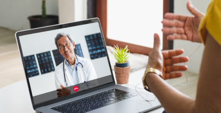 A doctor and their patient talk over a video call. The doctor is seen listening and smiling on screen.