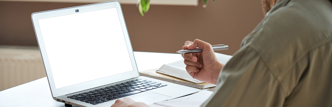 A person sits in front of a laptop screen and writes in their notebook.