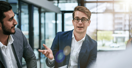 A group of professionals sit in a meeting. One person leads the conversation and the others listen.