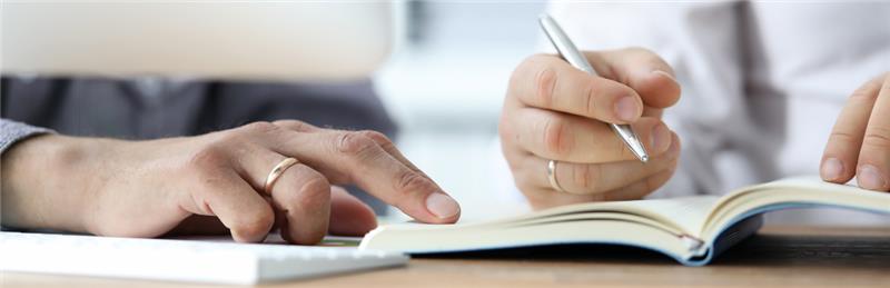 A close-up of two people's hands as they write in a notebook.