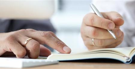 A close-up of two people's hands as they write in a notebook.