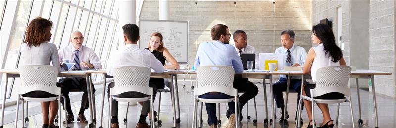 A team of people sitting at a long table in a modern office space.