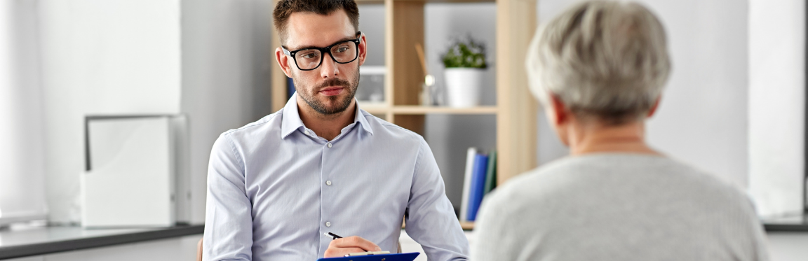 A practitioner is sitting down with their patient, attentively listening and writing down information on a clipboard.