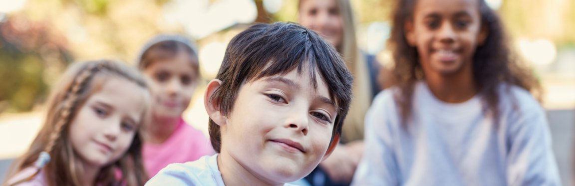 A child sitting outside with their friends. They all face forward and smile.