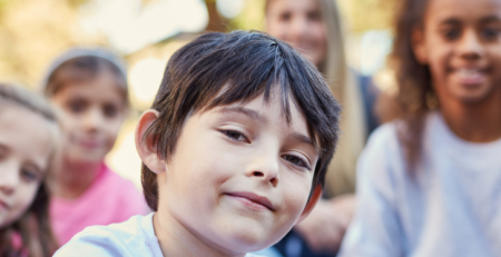 A child sitting outside with their friends. They all face forward and smile.