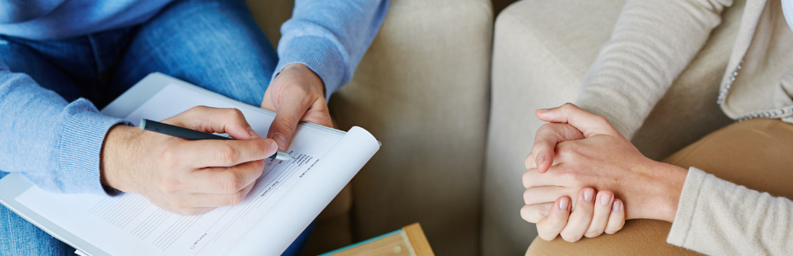 A psychologist is sitting down with their patient. The psychologist is filling out a form.