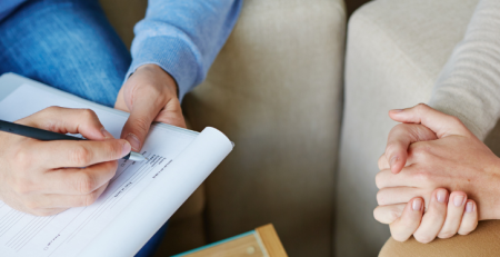 A psychologist is sitting down with their patient. The psychologist is filling out a form.