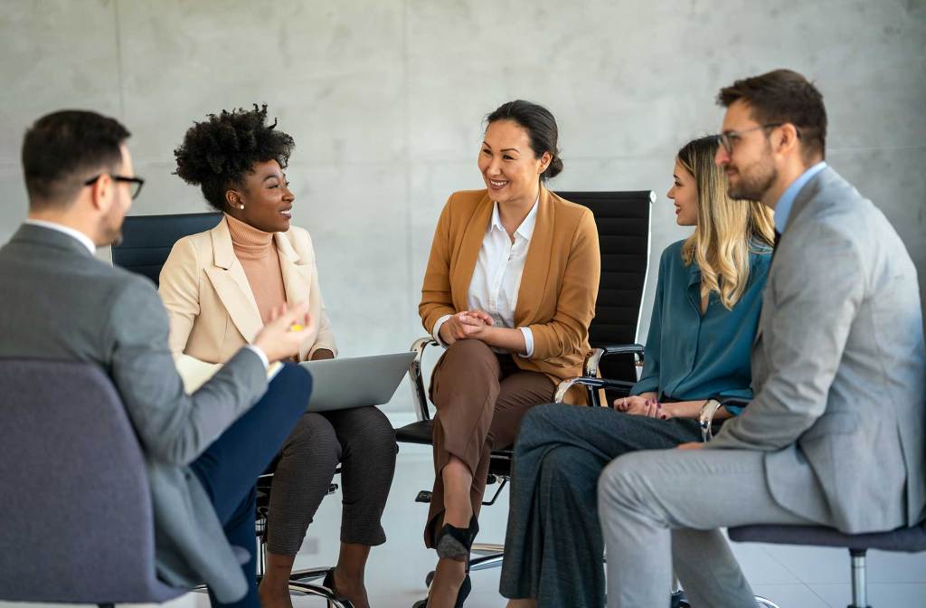 Group of professionals in a casual business meeting, smiling and engaged in discussion in a modern office.