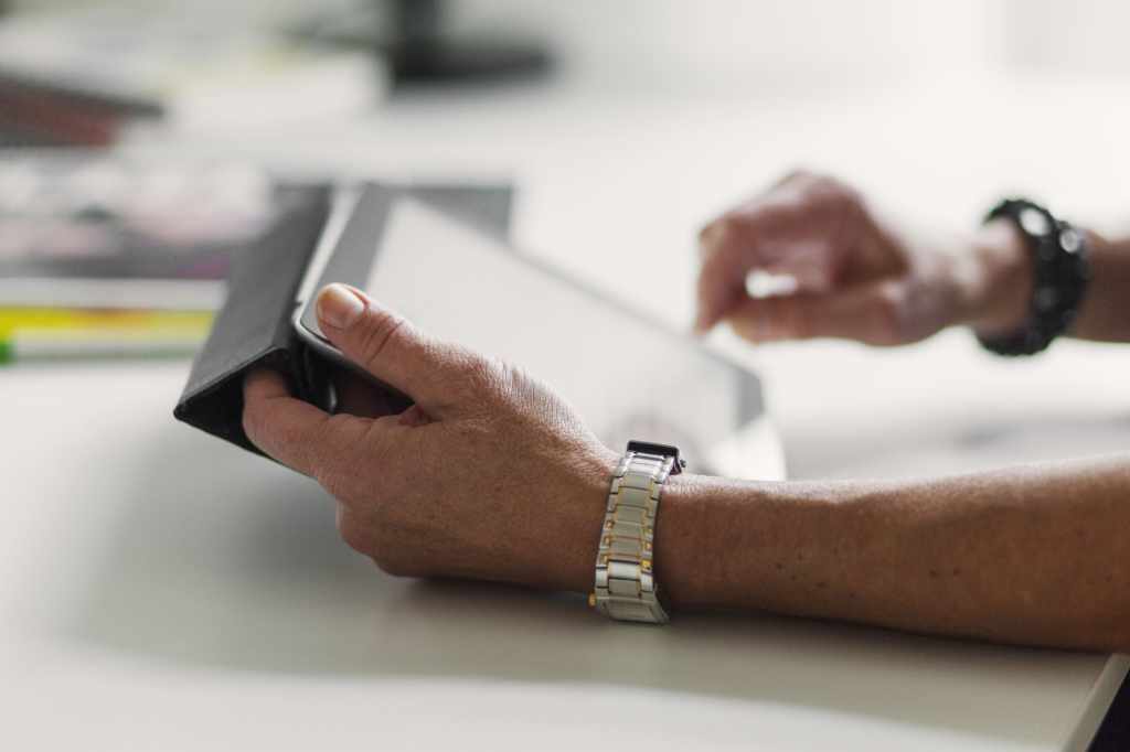 Close-up of a person’s hands writing with a pen next to a tablet on a desk, suggesting note-taking or documentation in a work setting.